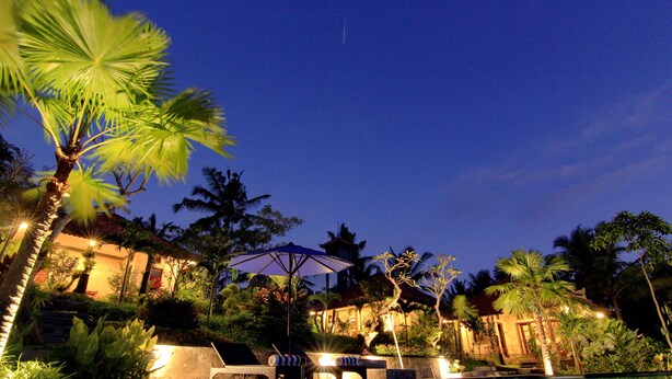 Un resort notturno con piscina, lettini e palme.