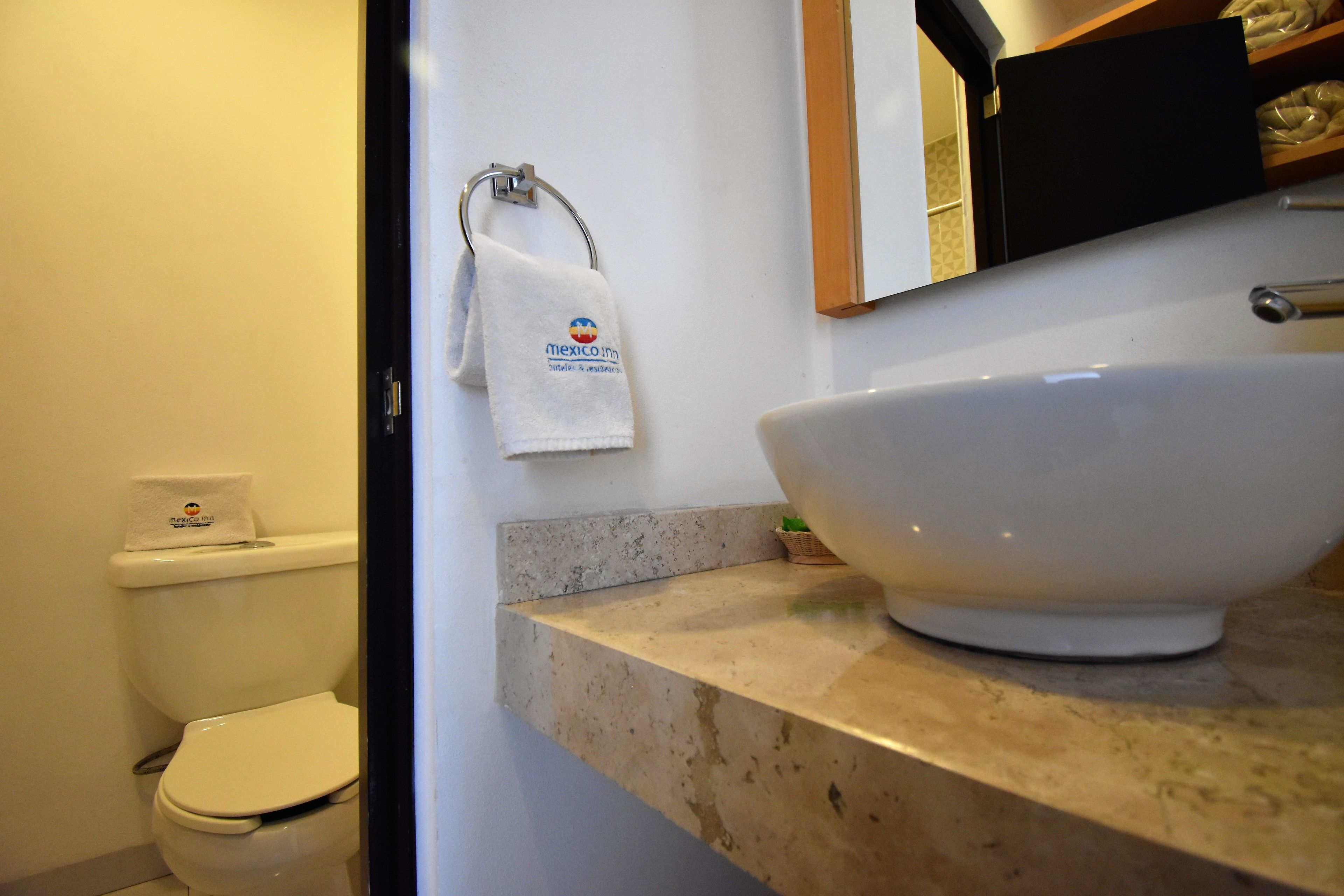 Un baño con inodoro blanco, un lavamanos blanco de gran tamaño y una toalla colgada en un aro metálico.