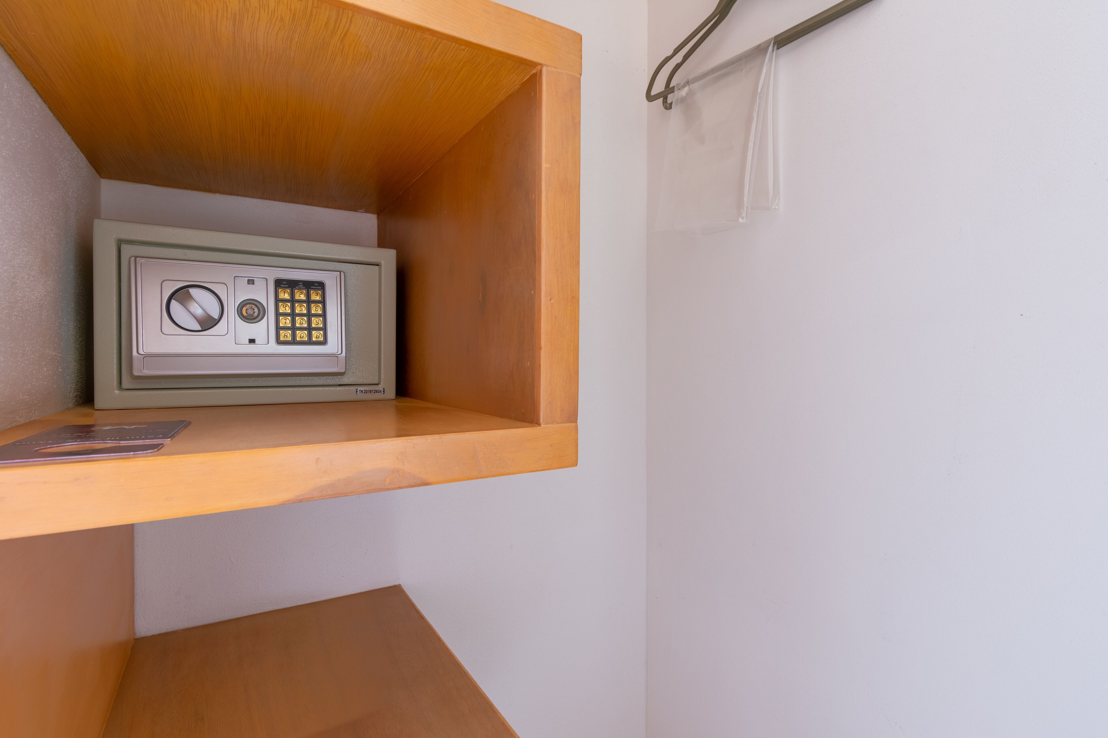 Un coffre-fort placé dans un coin d’une pièce, avec une étagère en bois et un mur blanc.