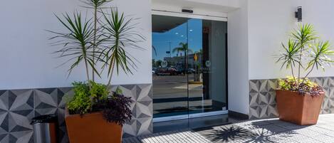 A modern hotel entrance with geometric patterned walls, potted plants, and a clear view of the street outside.