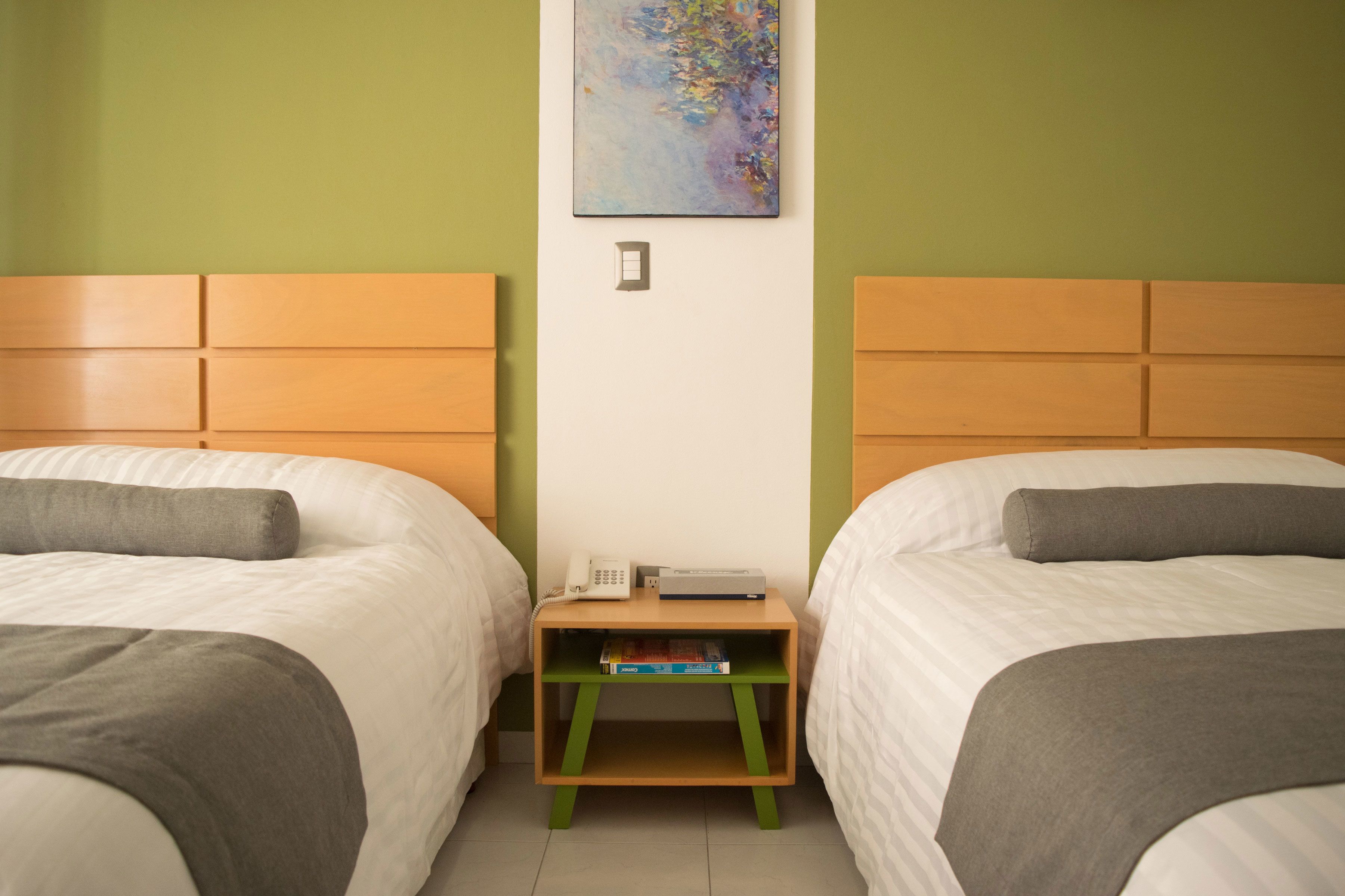 Habitación de hotel con dos camas, una mesita de noche de madera, un teléfono y un cuadro en la pared.