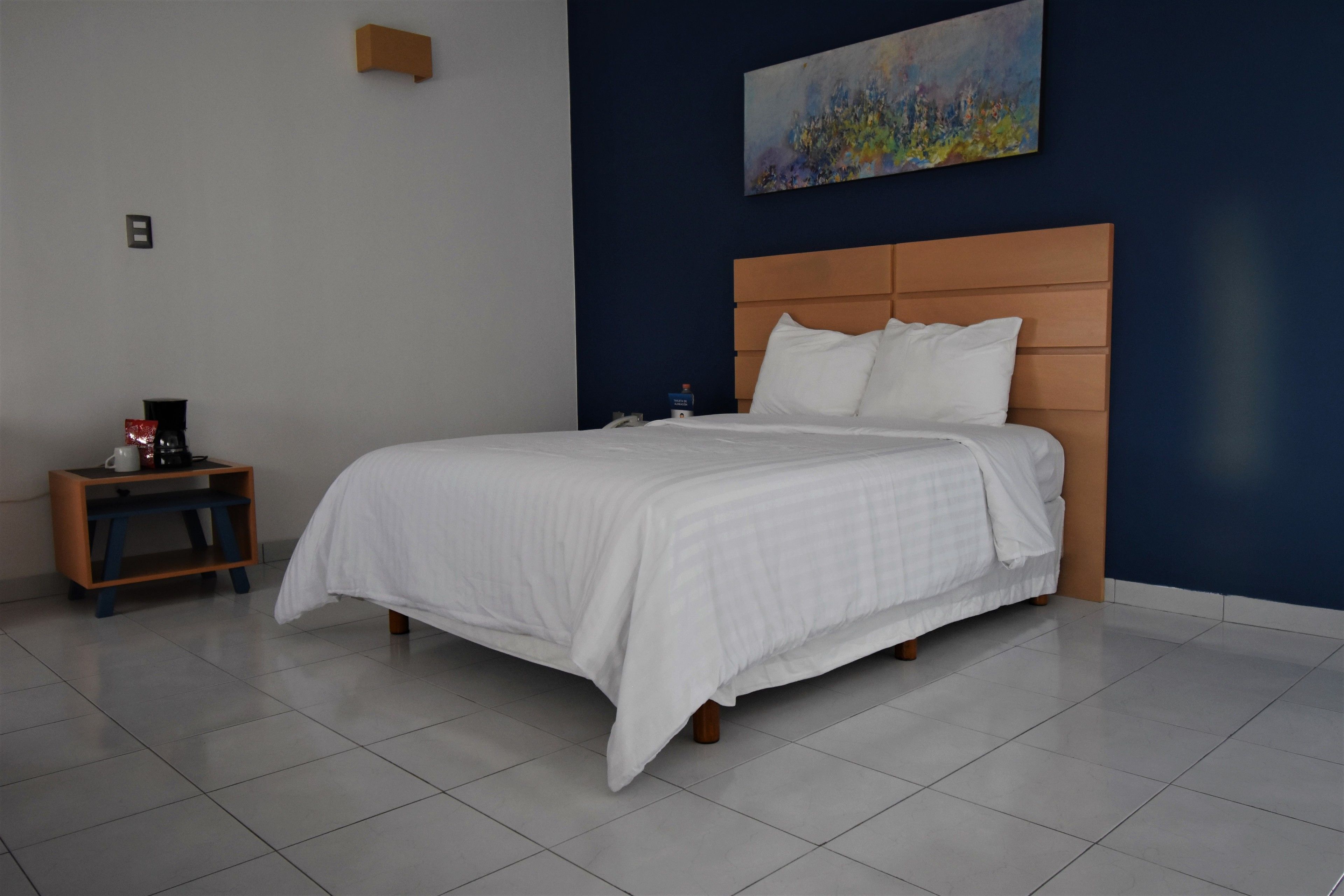 A neatly made bed with a wooden headboard in a room with a blue accent wall and a painting.