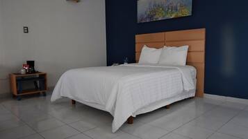A neatly made bed with a wooden headboard in a room with a blue accent wall and a painting.