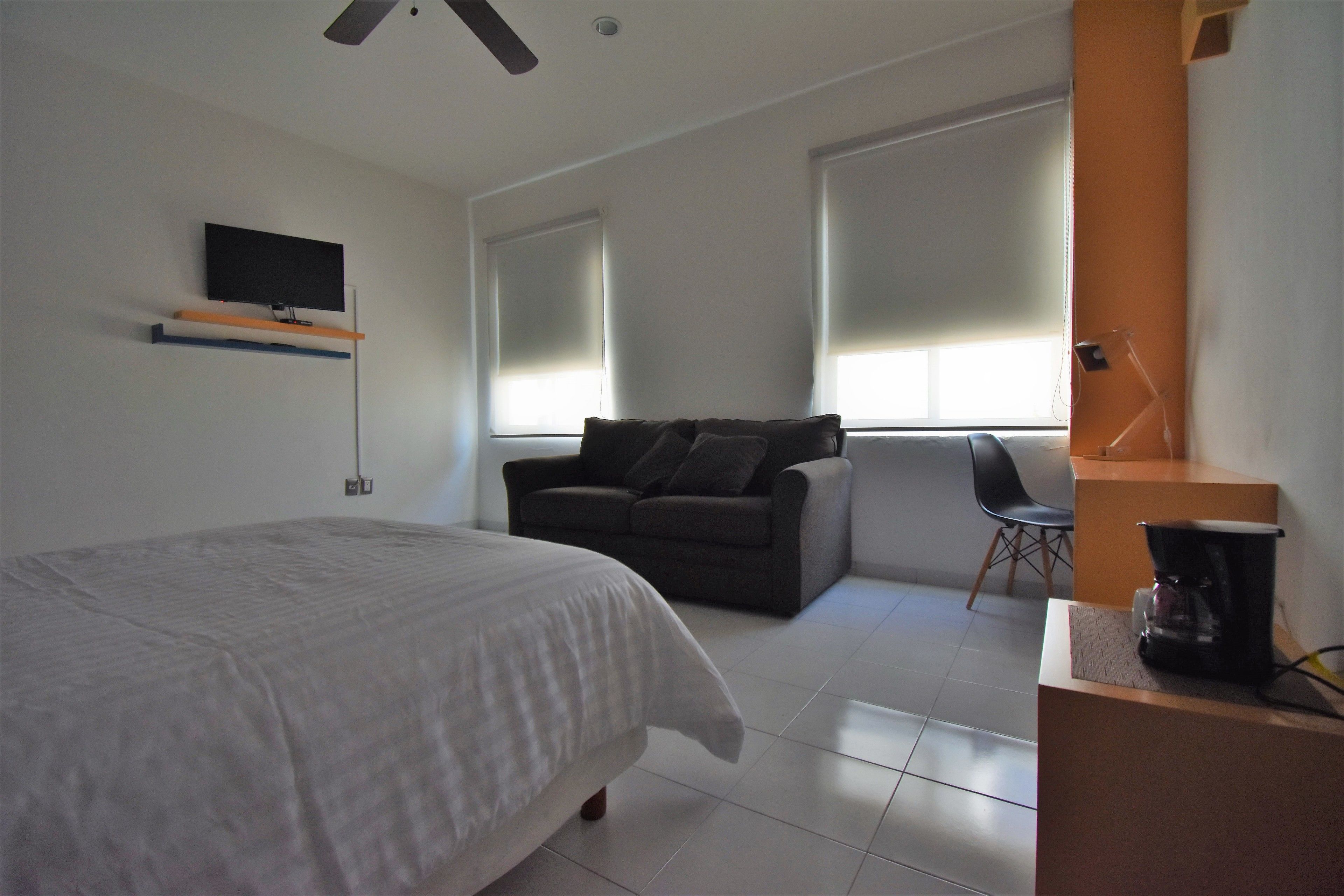 Quarto com cama, sofá, máquina de café e televisão na parede.