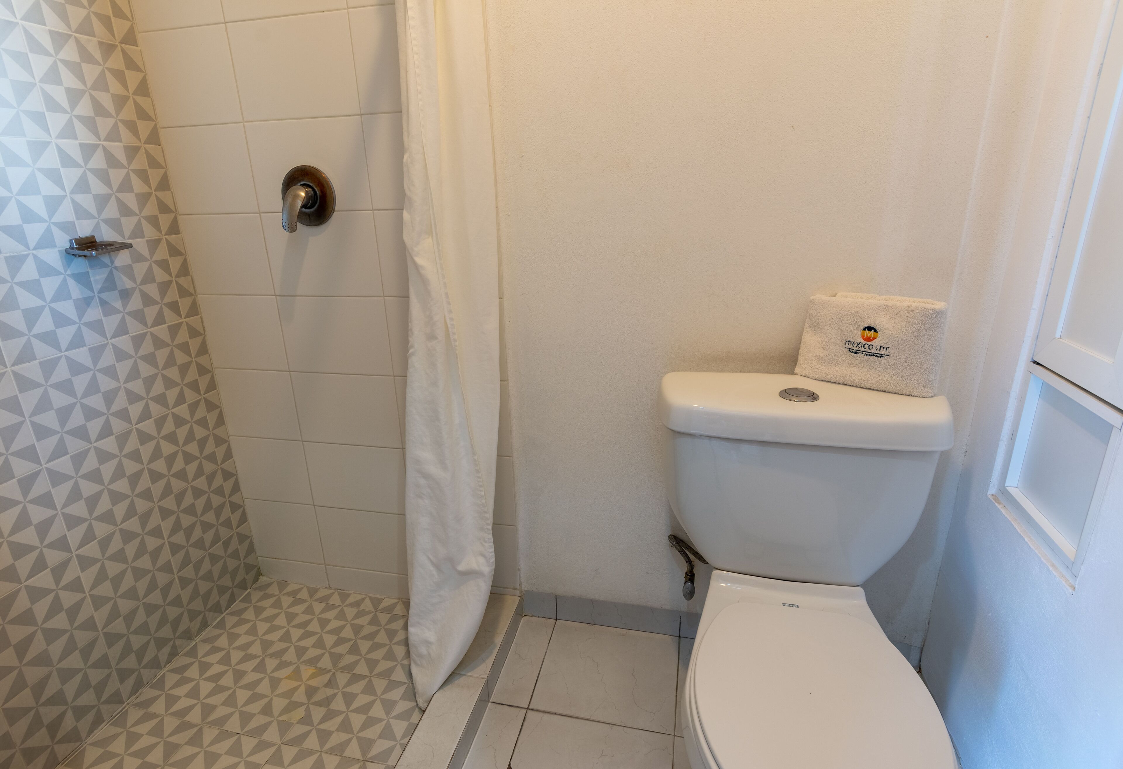 A bathroom with a toilet, a shower with a geometric tile pattern, and a towel with a logo.