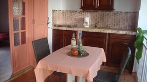 Uma sala de jantar com mesa posta para dois, uma cozinha com armários de madeira e painel de azulejos.