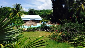Um resort com piscina, construções de palha e vegetação exuberante.