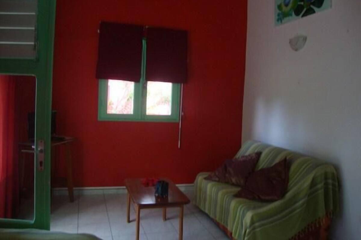 Una habitación con sofá verde, una mesita de madera y una ventana con cortinas.
