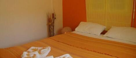 A neatly made bed with white linens and a striped orange bedspread.