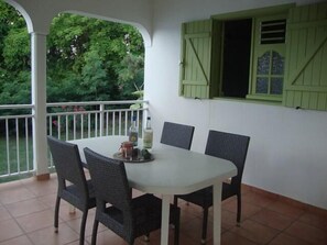 Un patio techado con una mesa blanca y cuatro sillas, una botella de agua y una copa de vino sobre la mesa.