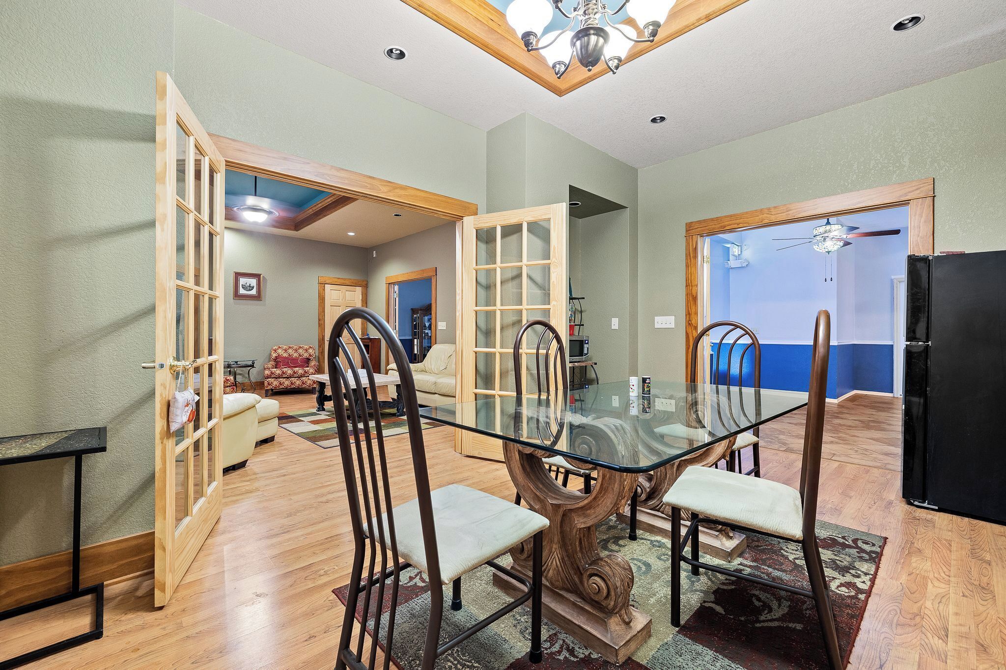 A dining area with a glass-top table, wooden chairs, and a wooden floor.