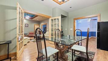 A dining area with a glass-top table, wooden chairs, and a wooden floor.