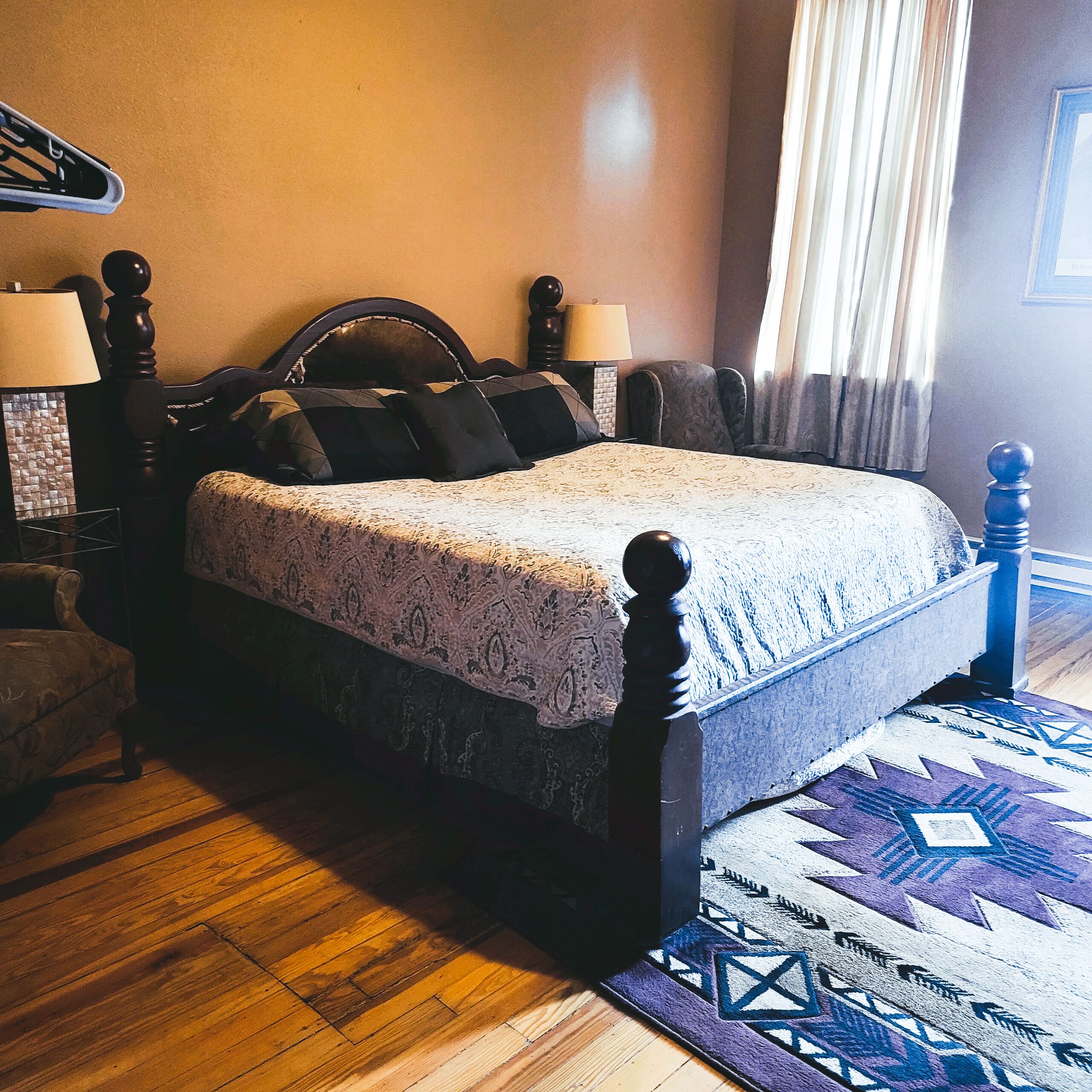 Una camera da letto con un letto in legno, un comodino, una lampada e un tappeto decorato.