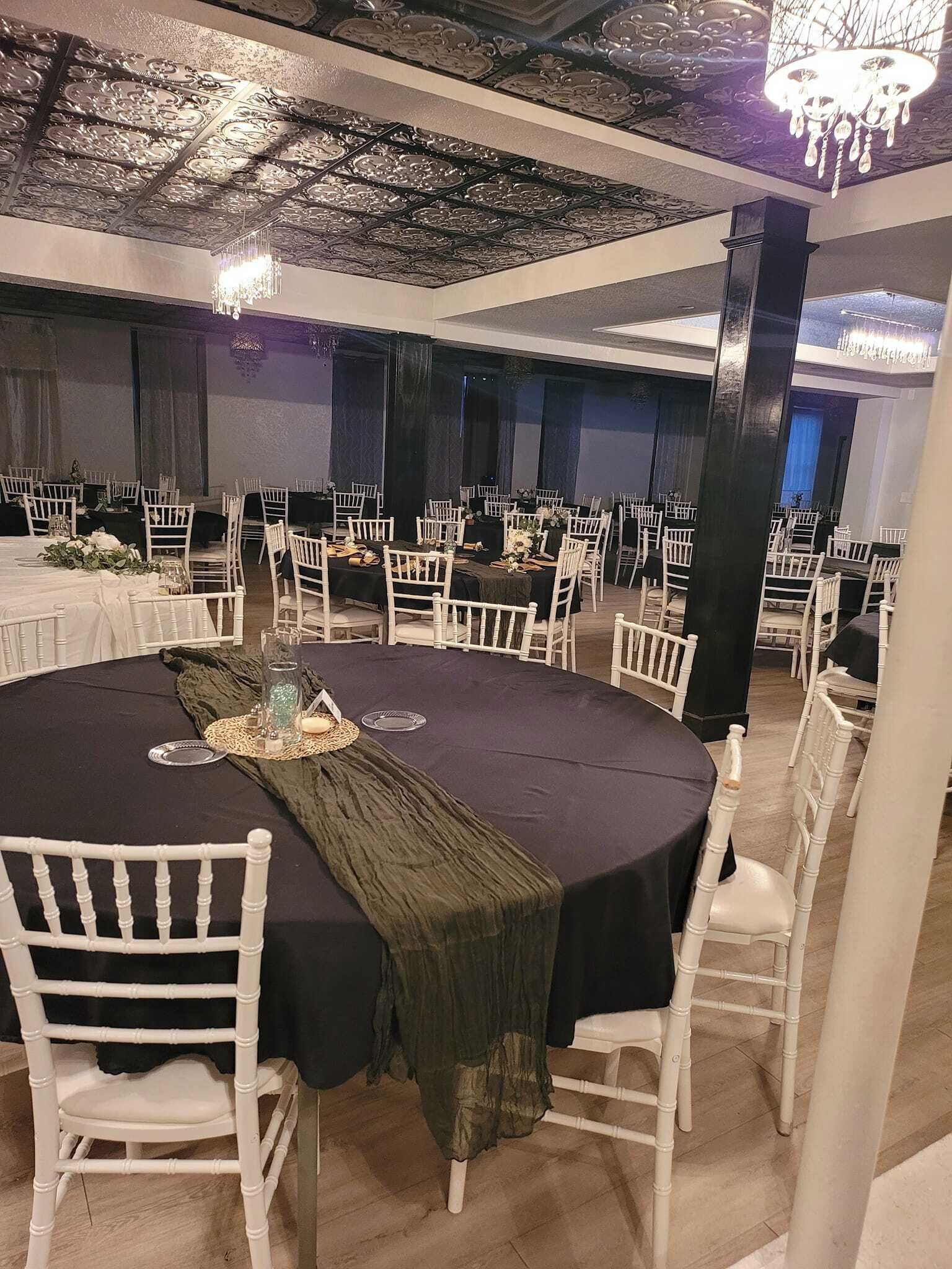 A banquet hall with round tables, white chairs, and black tablecloths.