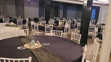 A banquet hall with round tables, white chairs, and black tablecloths.