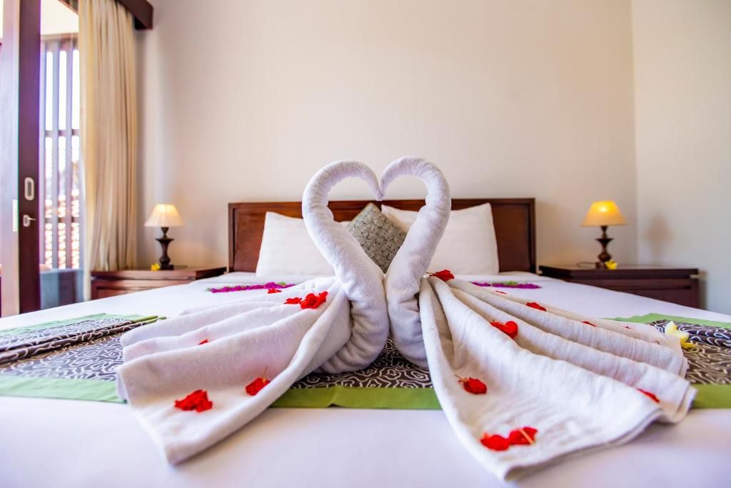 Una habitación de hotel con una cama, almohadas, una mesita de noche y una lámpara.