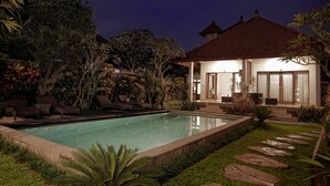 A swimming pool with lounge chairs, a well-maintained lawn, and a house with a tiled roof and large windows. - Lili Cottage Ubud (Ubud)