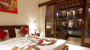 A hotel room with a bed, a nightstand, a lamp, a large window, and a view of a pool and outdoor area. - Lili Cottage Ubud (Ubud)