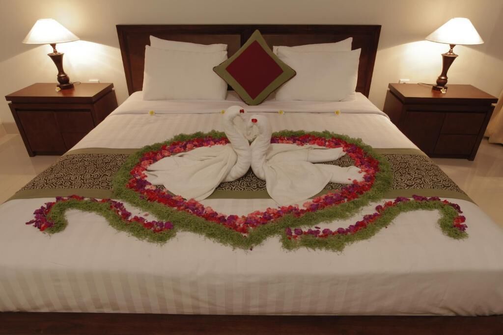 En pænt redt seng med blomsterarrangement i hjerteform og to svaner foldet af håndklæder.