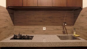 A kitchen with wooden cabinets, a granite countertop, a gas stove, and a stainless steel sink. - Lili Cottage Ubud (Ubud)