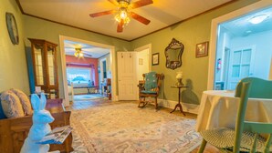 A cozy living room with a wooden floor, a patterned rug, a rocking chair, a table with a white tablecloth, and a ceiling fan. - The Maid's Quarters Bed Breakfast & Tearoom (Pottsville)