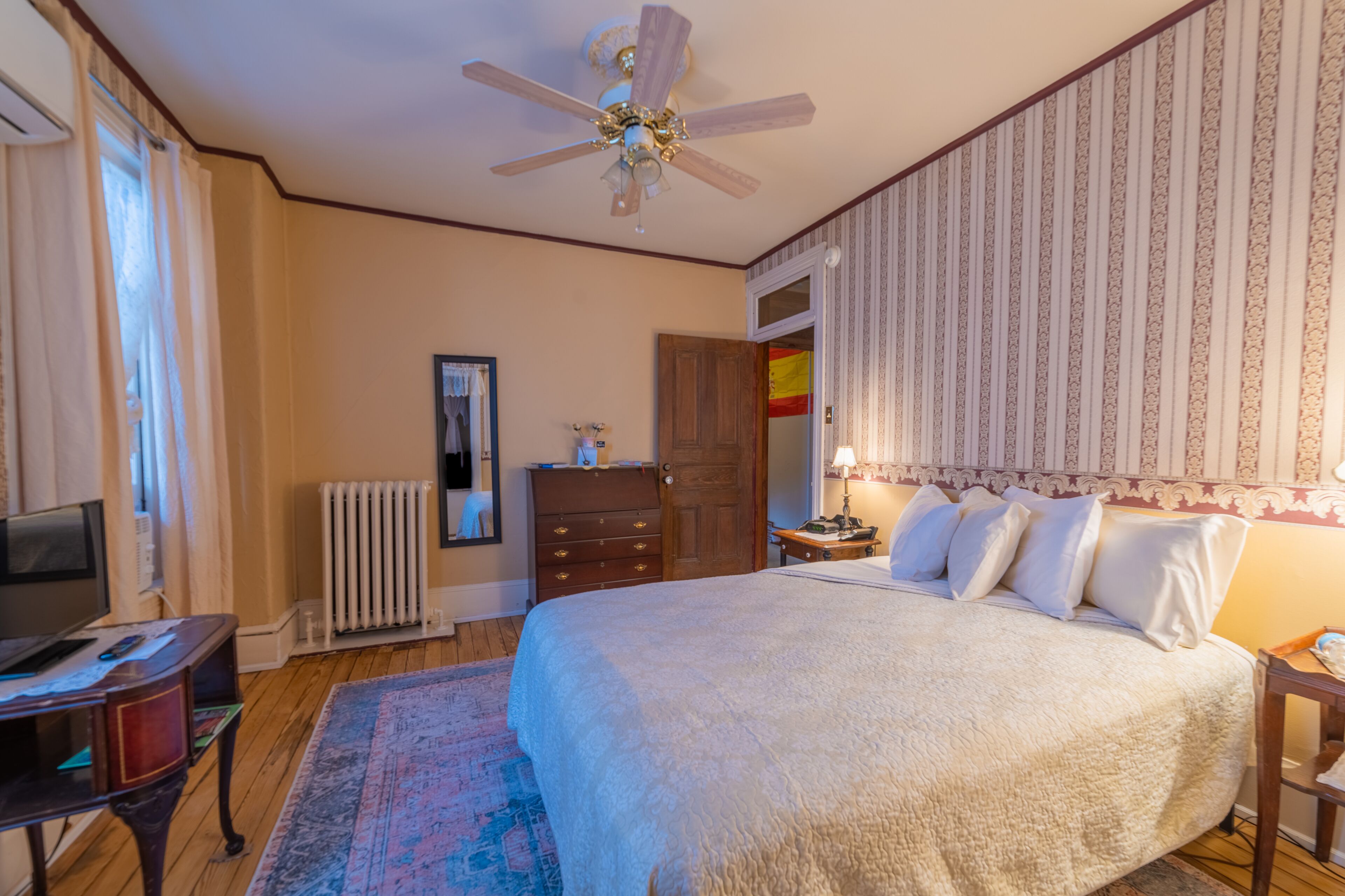 Un dormitorio con cama, ventilador de techo, cómoda, radiador y televisor.