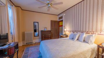 Un dormitorio con cama, ventilador de techo, cómoda, radiador y televisor.