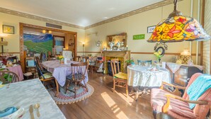 A cozy dining area with wooden tables and chairs, a fireplace, and a stained glass lamp. - The Maid's Quarters Bed Breakfast & Tearoom (Pottsville)