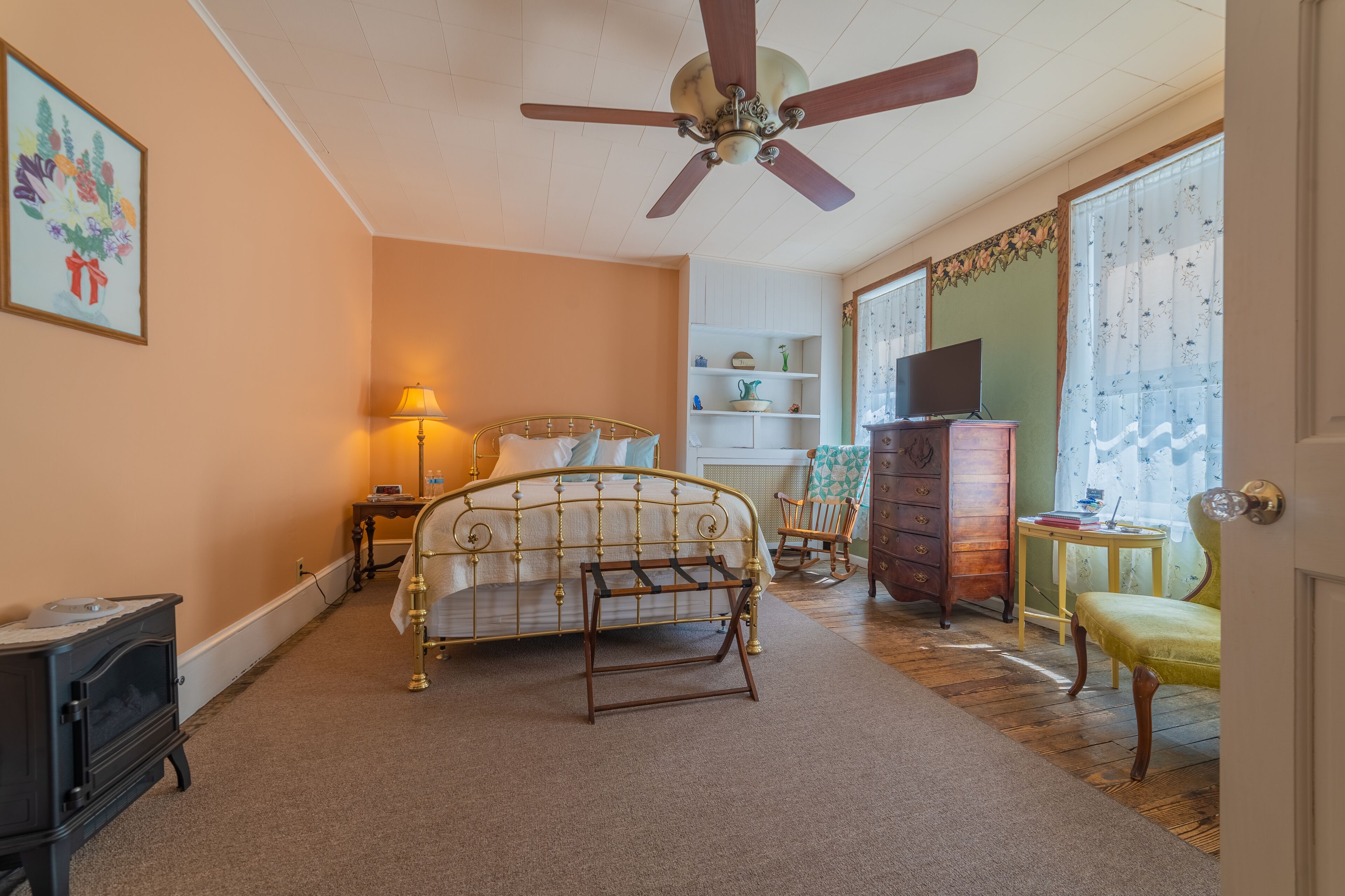 A bedroom with a bed, a dresser, a chair, a television, and a ceiling fan.