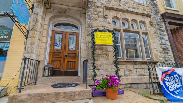 A stone building with a wooden door, a sign indicating it's open for breakfast, and a flower pot on the steps. - The Maid's Quarters Bed Breakfast & Tearoom (Pottsville)