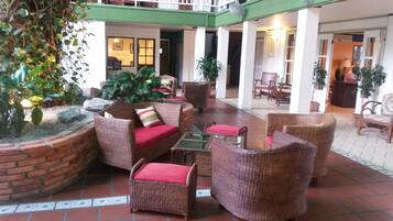 A covered outdoor seating area with wicker furniture and a brick planter with plants.