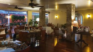 Un restaurante con mesas y sillas de madera, pilares de piedra y vistas al exterior.