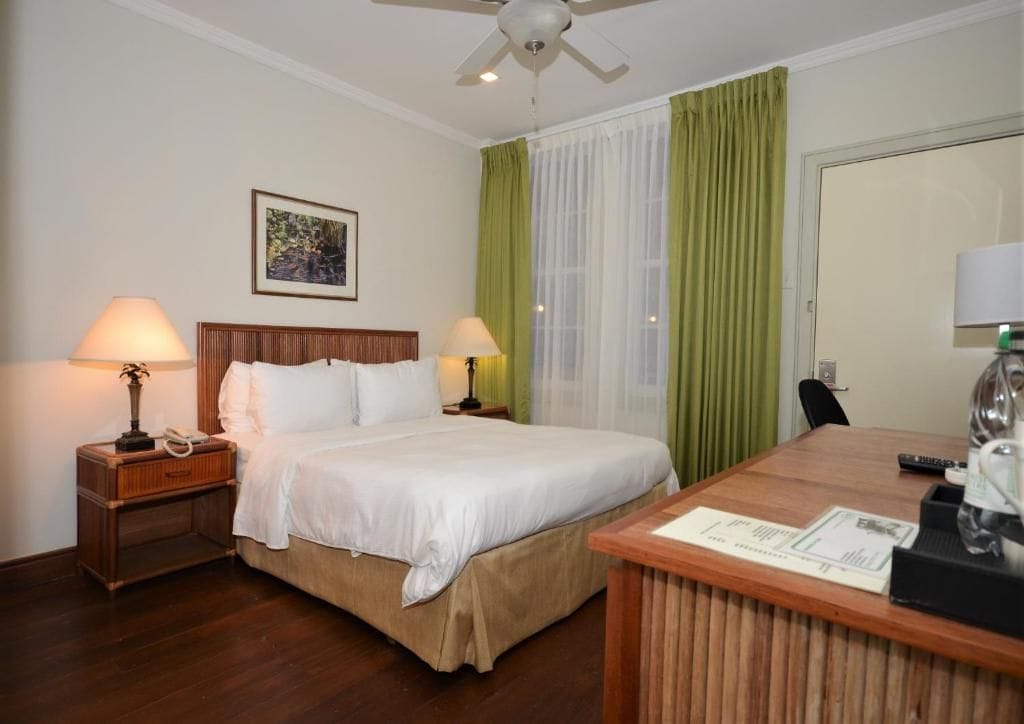 A hotel room with a bed, two bedside tables with lamps, a desk with a chair, and a ceiling fan.