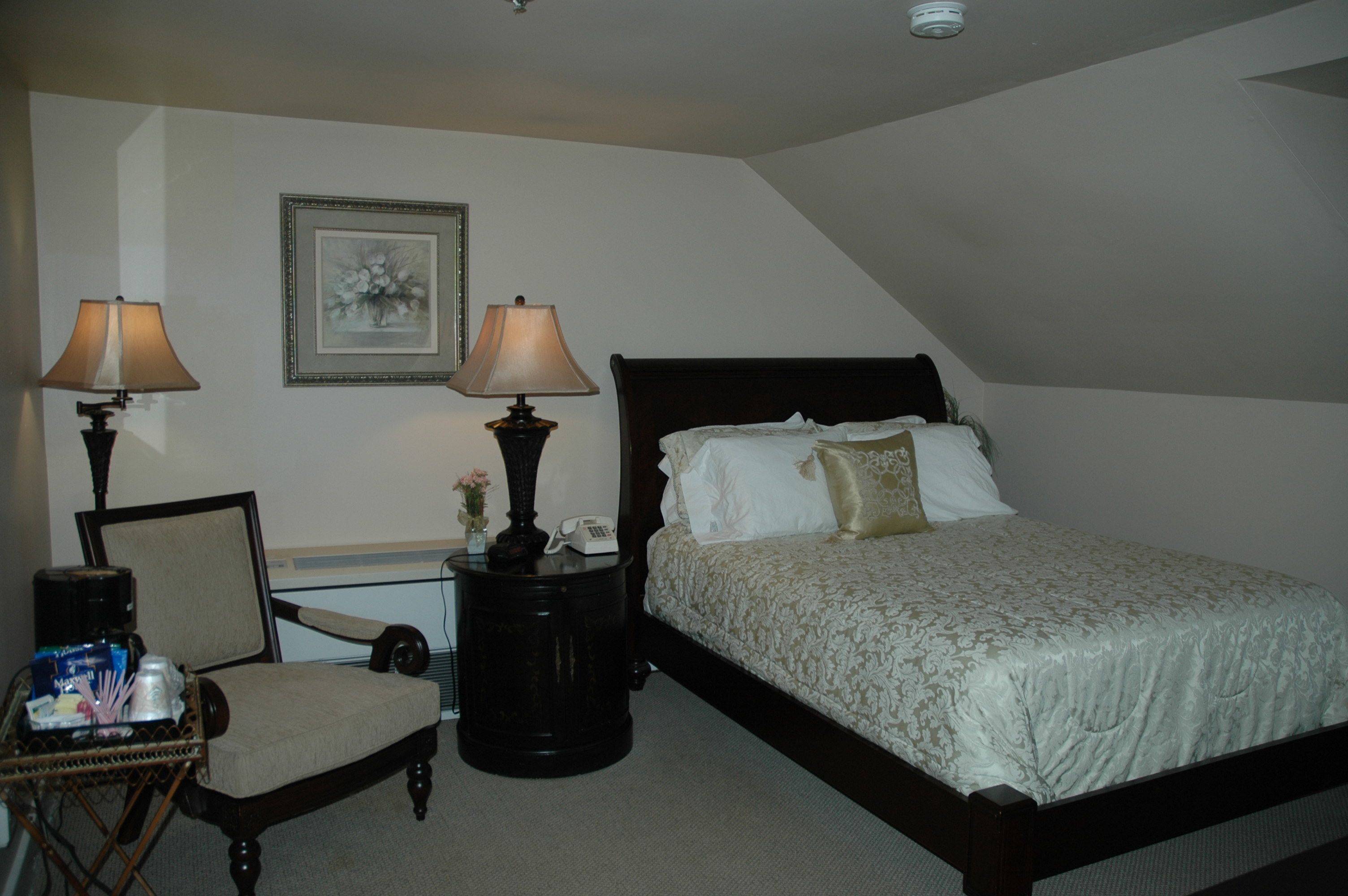 A bedroom with a bed, two bedside tables with lamps, a chair, and a framed picture on the wall.