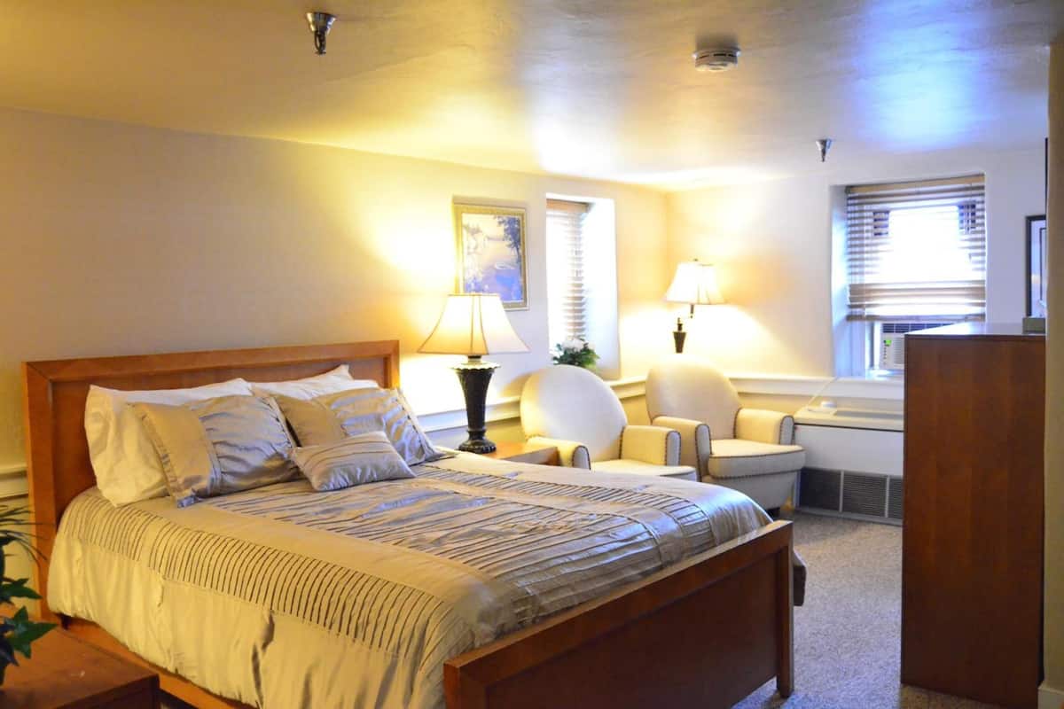 A neatly arranged bedroom with a large bed, two bedside lamps, a chair, and a desk.
