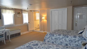 A bedroom with two beds, a desk, and a chair. There is a door leading to another room and a lamp in the corner.