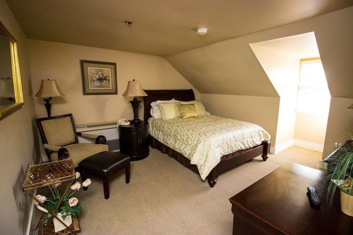 A bedroom with a bed, bedside lamps, a chair, a small table, and a decorative plant.