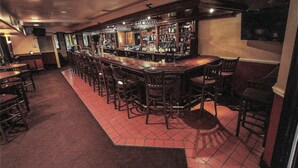 Eine Bar mit mehreren Hockern und einer langen Theke, ausgestattet mit verschiedenen Flaschen und Gläsern.