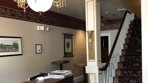 Ein Empfangsbereich mit dunklem Holzbüro, einer Kristallleuchter, gerahmten Kunstwerken und einer Treppe mit gemustertem Teppich.