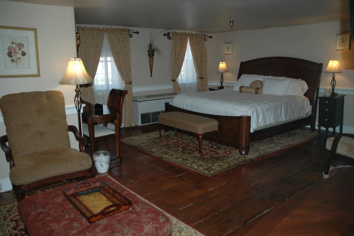 A bedroom with a large bed, two bedside tables, a chair, a bench, and a small table with a lamp.