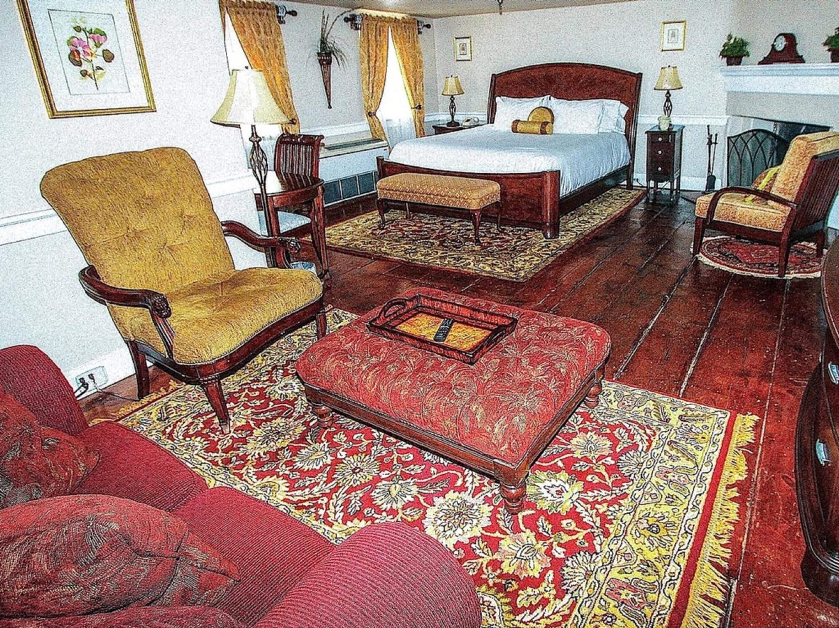 A traditional room with a large bed, a wooden armchair, a red sofa, and a patterned rug.