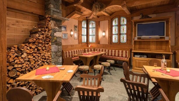 Interior acogedor de una cabaña de troncos con chimenea de piedra, bancos de madera y un televisor.