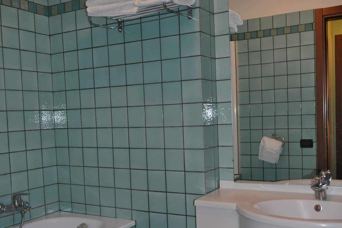 A bathroom with teal tiles, a sink, a mirror, and a towel rack.