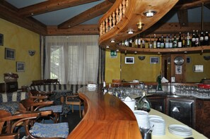 A bar area with wooden furniture, a curved bar, and a variety of bottles and glasses.