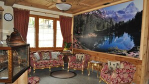 Una habitación con un cuadro grande de montañas, techo de madera y un conjunto de sofá con estampado rojo y dorado.
