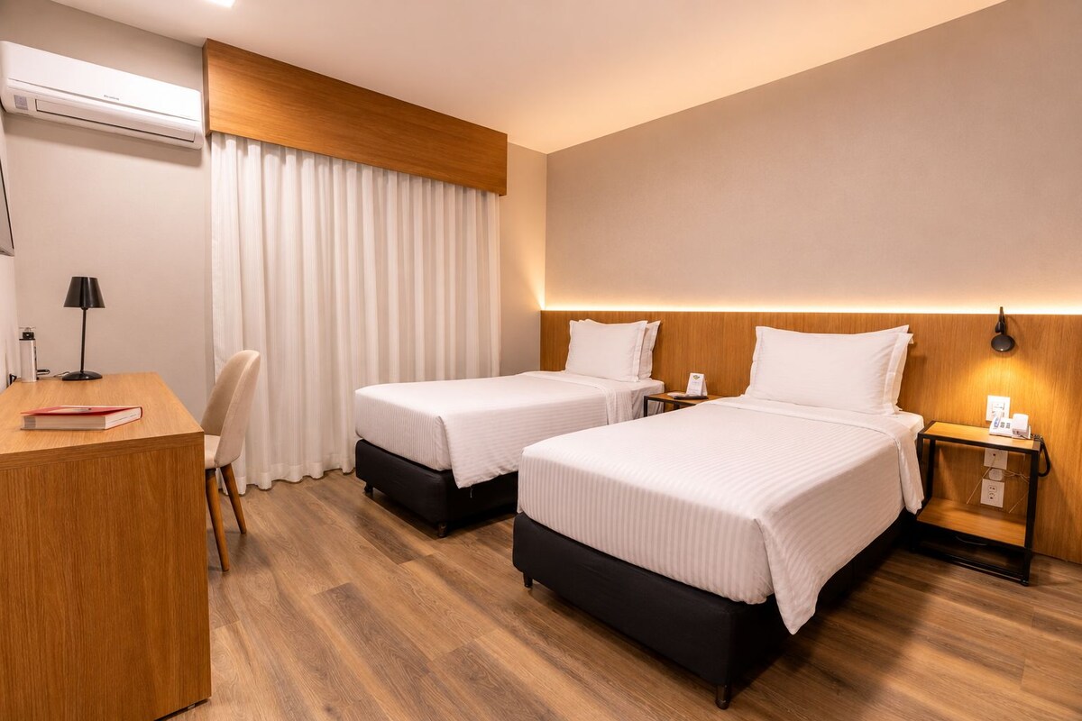 Une chambre d’hôtel avec deux lits, un bureau, une chaise, une lampe et une table de chevet avec un téléphone.