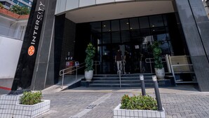 Moderne hotelentree met een glazen gevel, een opvallend logo en een trap naar de lobby.