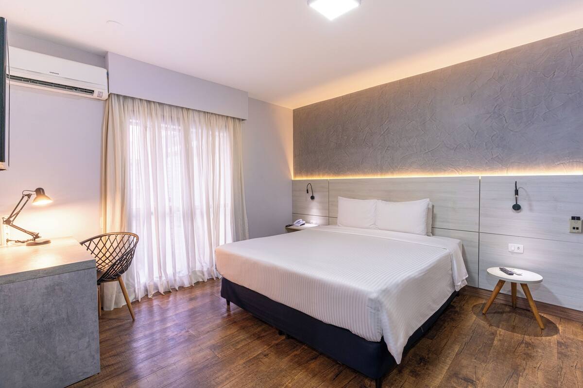 Una habitación de hotel moderna con una cama grande, mesitas de noche, un escritorio con lámpara y una silla.
