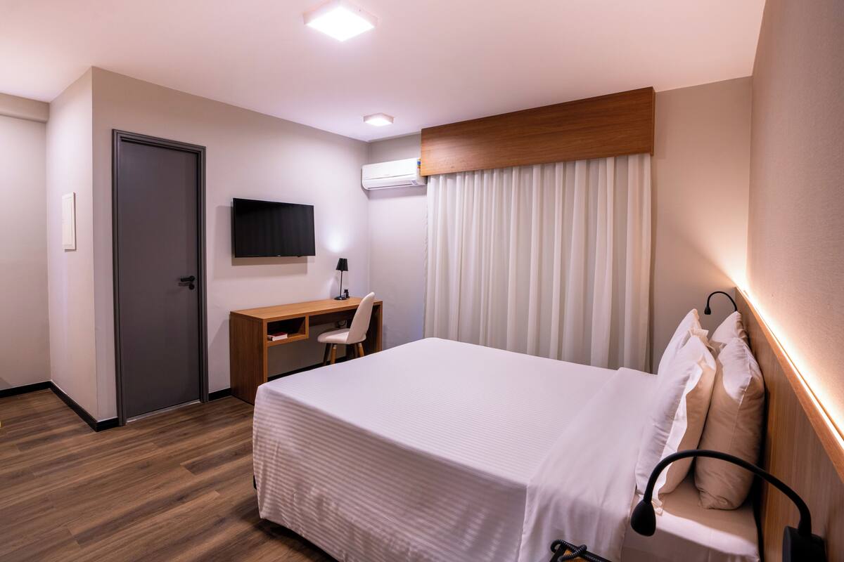 Una habitación de hotel con cama, escritorio, silla y televisor en la pared.