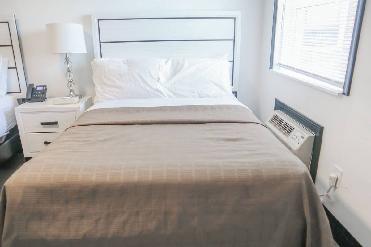 Un lit bien fait, recouvert d’une couvre-lit beige, une table de chevet avec une lampe, un téléphone et une petite boîte.